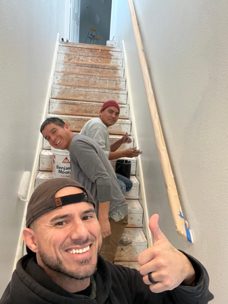 Three individuals working together to renovate a staircase with paint and tools.
