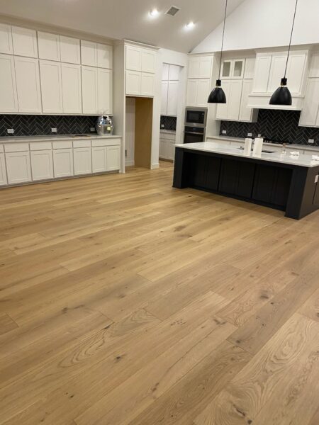 A spacious modern kitchen featuring light hardwood floors, white cabinets, and dark accents.